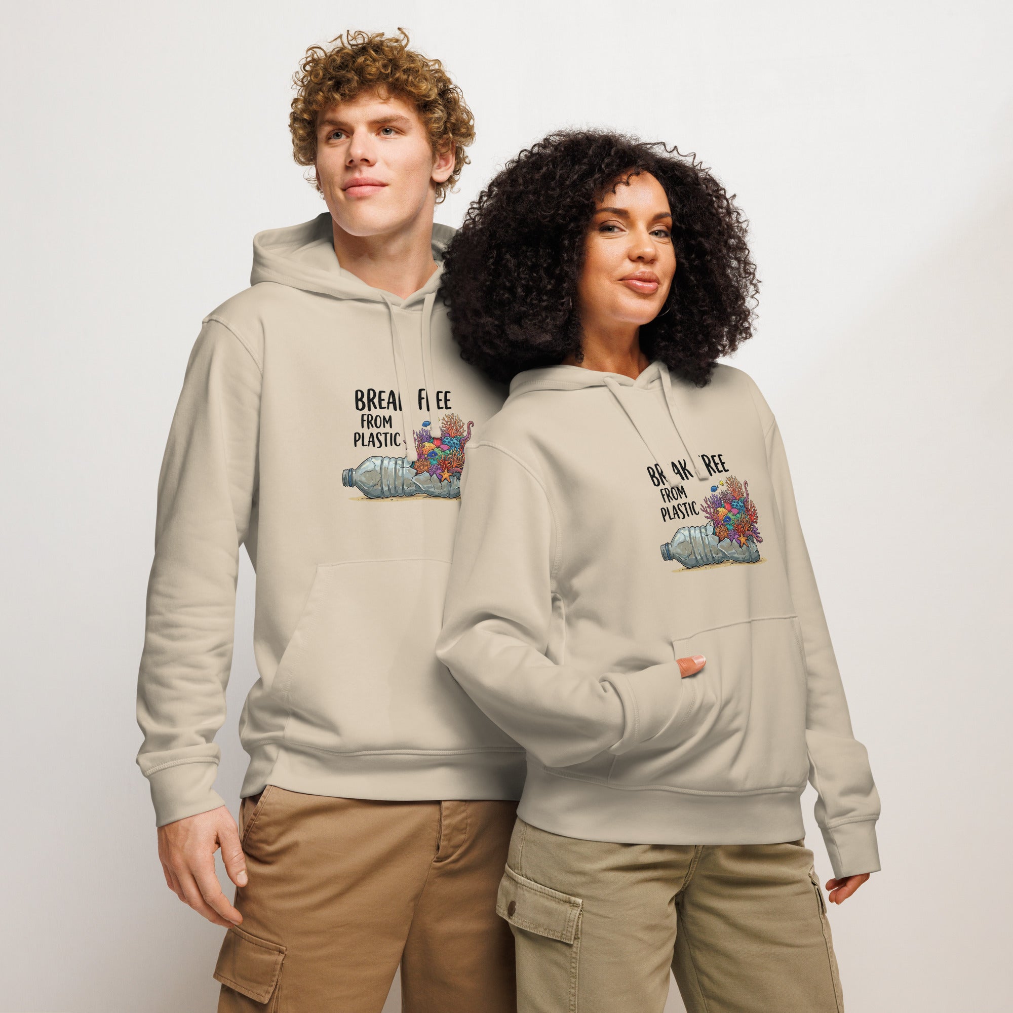 A man and a woman standing together against a white background, both wearing sand-colored hoodies featuring a graphic of a plastic bottle with colorful coral growing out of it and the text "BREAK FREE FROM PLASTIC."