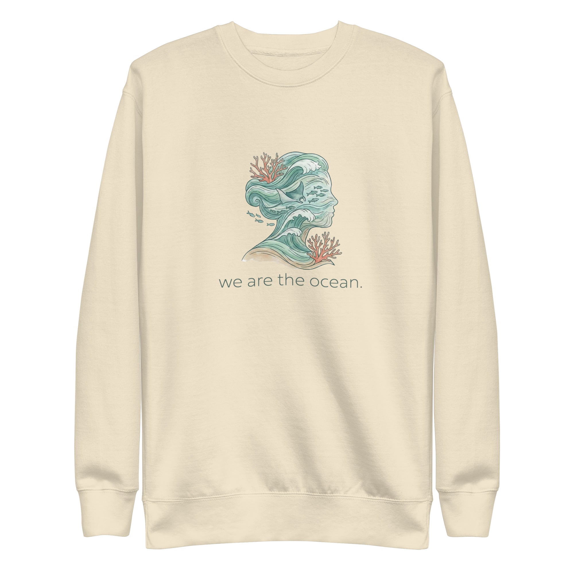 A high-resolution front view of a beige organic hoodie. The central graphic features an artistic silhouette of a human profile filled with teal ocean waves, a stingray, and small fish, accented by orange coral. The text "we are the ocean." is printed in a clean font below the illustration.